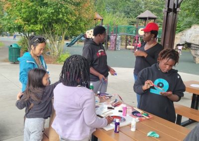 Group of people painting at table with playground in background